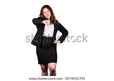 Young chubby office manager is showing thumbs down. Woman wears black strict lady suit. Her hair is brown and loose. Isolated, white background.