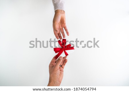 Beautiful holiday or Christmas background image of a Caucasian male's hand giving a small red ribbon wrapped gift box to a mixed race African American woman wearing a sweater with copy space.