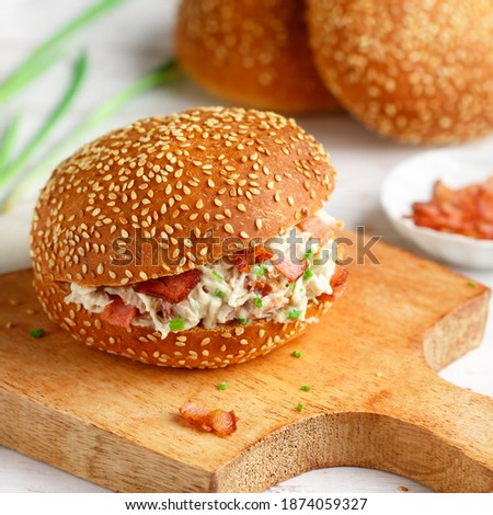 Delicious sesame bun sandwich with chicken salad, fried bacon, green onions, cheese with ranch sauce. Lunch or dinner for gourmets. Selective focus, square picture,