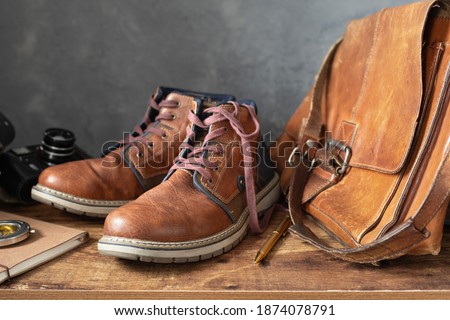old travel vintage boots shoes and leather bag at wooden table, with wall background texture