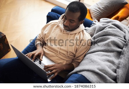 Overhead view of young mixed ethnicity man lying on sofa at home using laptop computer to work from home or shop online