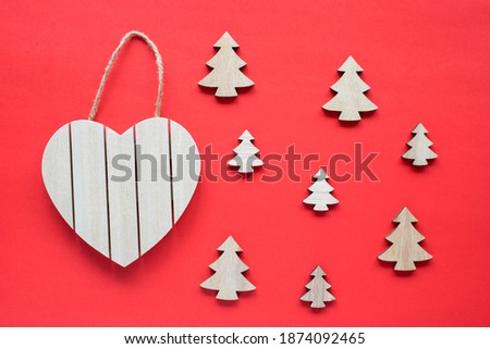 Heart shape wooden sign board frame hanging on a rope and little fir trees on red background.Eco friendly christmas holiday concept