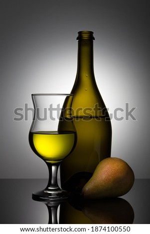Stylish, modern still life with glass objects (a wine bottle and a wine glass) and an ripe juicy pear.