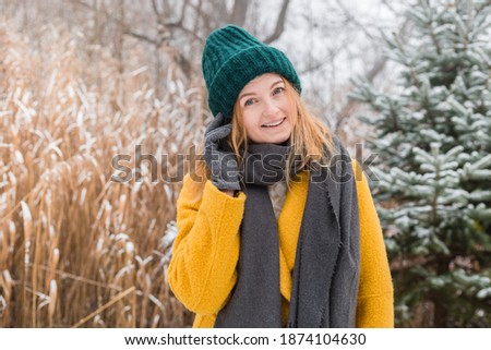Happy young woman wearing a coat, hat and scarf smiling over nature background, trendy color of year 2021 - illuminatiing yellow and ultimate gray, winter time