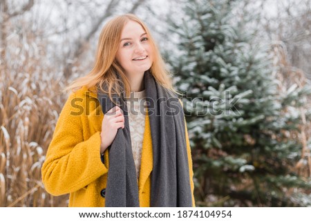 Happy young woman wearing a coat and scarf smiling over nature background, trendy color of year 2021 - illuminatiing yellow and ultimate gray, winter time