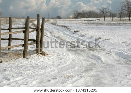 A rural snow-covered landscape with a wooden fence and a road going over the horizon with clouds in the background on a clear frosty day. Winter vacation in Russia.