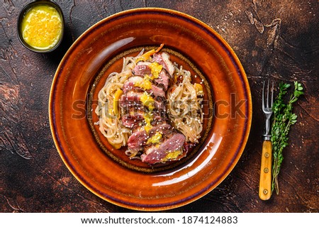 Noodles with duck breast fillet steak on a plate. Dark background. Top view