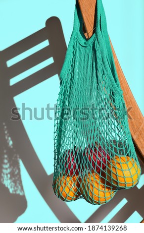 Cloth bag with fruit on the back of the chair, reusable material for natural products. Conscious consumption concept without plastic waste. Close-up, sunlight, blue background