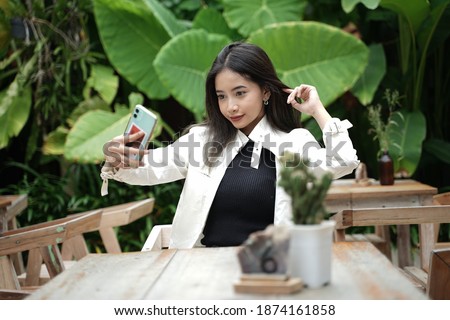 Young woman taking a selfie using a smartphone. the model is styled like a model with a beautiful garden setting. the evening light adds to the beauty of the model when captured.