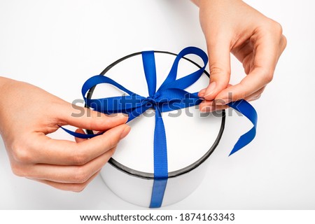 hands untie the ribbon on the gift box. the girl opens a gift. gift round white box with a blue bow on a light background. surprise for christmas and new year. birthday present macro top view