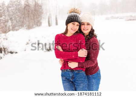 TWO GIRLS IN RED SWEATERS IN THE WINTER FOREST. THE SISTERS WALK IN THE SNOW IN THE PARK