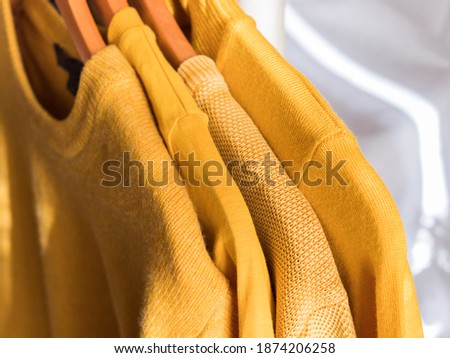 Yellow illuminated color winter sweaters on wooden hangers. Trendy fashion autumn warm and cozy clothes.