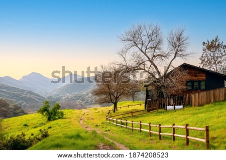 Beautiful southern California rural landscape, with fenced wooden hut on a green meadow and hazy mountains background.