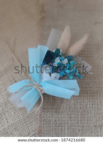 Tiny dried flowers bouquet wrap in blue paper on natural burlap