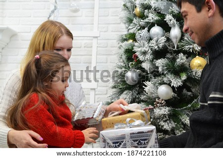 happy family, mom dad and little daughter give gifts to a friend near an elegant Christmas tree Young mother and her daughter opening a magical Christmas gift in cozy living room in winter. New year