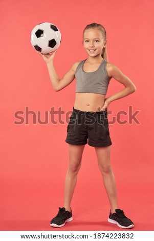 Cute female child with soccer ball standing against red background