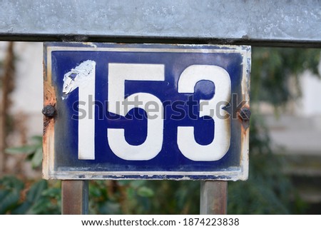 A blue house number plaque, showing the number one hundred fifty three (153)