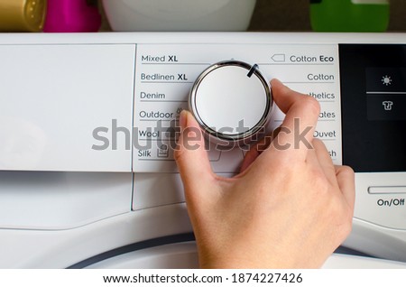 Hand turning the knob of the tumble dryer to adjust the temperature. Royalty-Free Stock Photo #1874227426