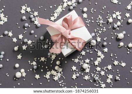 Stylish festive composition with gift box with pink pastel ribbon on trendy grey background with shining decorations. St. Valentine’s Day concept.