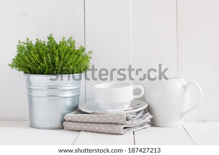 Cottage life, country kitchen decoration: a house plant in a metal pot, kitchen pottery, utensils and napkins on white painted board. Cozy home country life background is. Royalty-Free Stock Photo #187427213