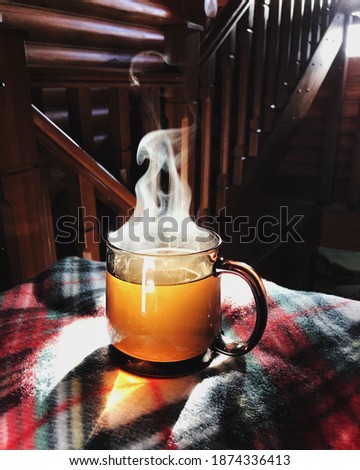 a cup of tea with steam stands on a plaid blanket