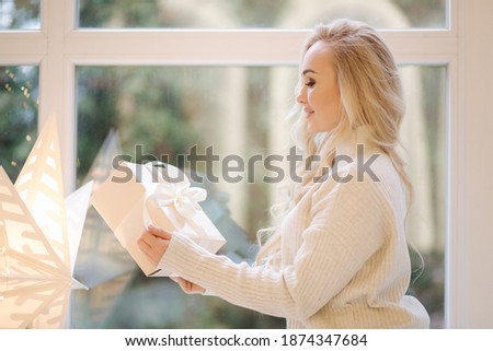 Portrait of Beautiful blond hair woman in pullover open present on Chrisrmas time. Elegant woman by Christmas tree. Attractive female hold present. Christmas mood