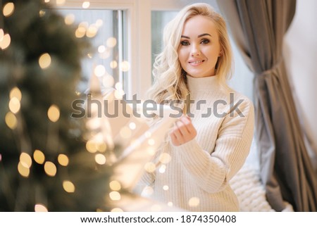 Portrait of Beautiful blond hair woman in pullover open present on Chrisrmas time. Elegant woman by Christmas tree. Attractive female hold present. Christmas mood. Winter holiday