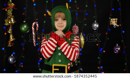 Little blonde kid teen teenager girl in Christmas elf Santa helper costume posing isolated on black background. Child dancing, fooling around, making funny faces. People New Year holidays celebration