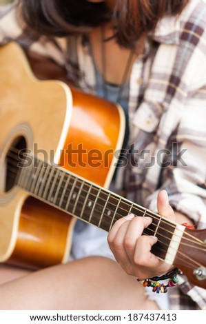 Closeup of young woman's hands playing acoustic guitar outdoors