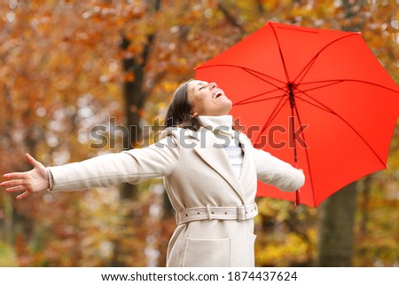 Happy fashion adult woman with umbrella celebrating autumn stretching arms in a park