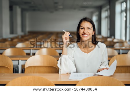 Knowledgable smiling student taking an easy exam in an empty amphitheater. An optimistic student taking an in-class test. Happy woman having stress free education evaluation.Essay exam inspiration. Royalty-Free Stock Photo #1874438854
