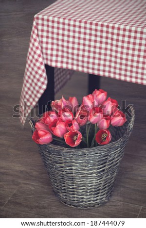 Vintage rustic photo of bouquet of spring tulips in a wicker basket on wooden floor