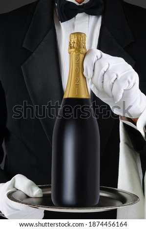 Closeup of a Sommelier holding a Champagne bottle, dated 2021 for the New Year on a silver tray. Man is unrecognizable, Vertical Format. Royalty-Free Stock Photo #1874456164