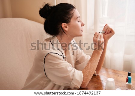 Time for me. Portrait of the nice attractive cheerful girl with vitiligo making fashionable manicure at home work place station near the window Royalty-Free Stock Photo #1874492137