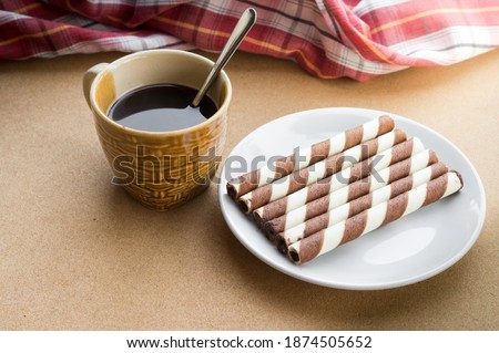 Chocolate wafer rolls with black coffee on table.