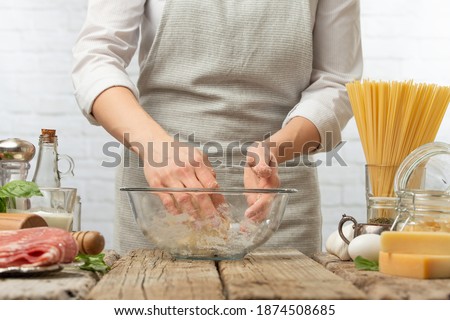 Professional chef mix ingredients with hands in glass bowl for cooking pasta alla carbonara. Backstage of preparing traditional italian dish on white background. Frozen motion. Cookbook illustration.