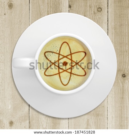 Cup of coffee standing on a wooden surface. Picture of the atom sign in the coffee crema. top view