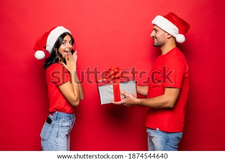 Happy couple in Santa hat gives gift, isolated on red background.