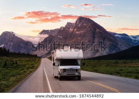 Scenic road in the Canadian Rockies during a vibrant sunny summer sunrise. White RV Driving on route. Taken in Icefields Parkway, Banff National Park, Alberta, Canada. Royalty-Free Stock Photo #1874544892