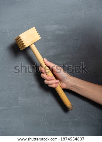 meat beater in a woman's hand on a gray textured background. Kitchen tools, vertical photo