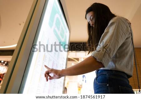 Navigation info panel in the shopping center, building plan with the layout of stores. A young female customer uses a touchscreen