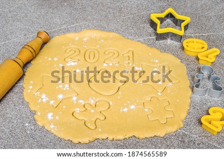 Preparing to make homemade cookies. On the yellow dough sprinkled with flour on top, the numbers 2021 are carved and various figures from the dough next to a rolling pin and yellow forms with numbers