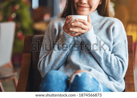 Closeup image of a beautiful young asian woman holding and drinking hot coffee in cafe