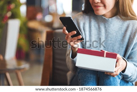 Closeup image of a beautiful young asian woman using mobile phone while holding gift box