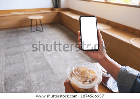 Mockup image of a woman holding mobile phone with blank white desktop screen while drinking coffee 