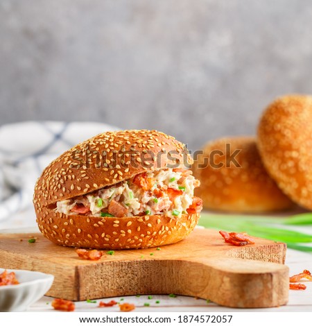 Delicious sesame bun sandwich with chicken salad, fried bacon, green onions, cheese with ranch sauce. Lunch or dinner for gourmets. Selective focus, square picture, copy space