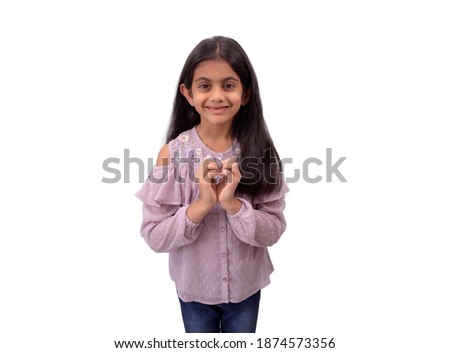A cute little indian girl with long hair showing heart shape sign with hands and expressing love.