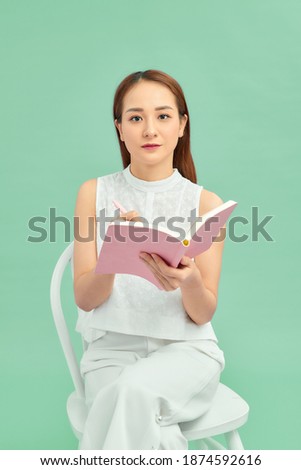 A young asian woman sitting and writing her notes isolated over blue background