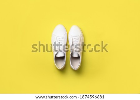 Stylish white sneakers on yellow background. Minimal flat lay. Demonstrating trendy Color of the Year 2021. Illuminating Yellow and Ultimate Gray.