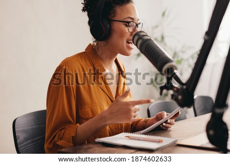 Female podcaster recording and broadcasting her podcast from home. Woman working from home reading a notepad and talking into a microphone.